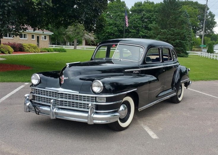 1948 Chrysler Windsor, fekete 4 ajtós limuzin, osztott szélvédő, háttérben kertvárosi kert, elölnézet, oldalnézet, balról döntve, alulról fotózva