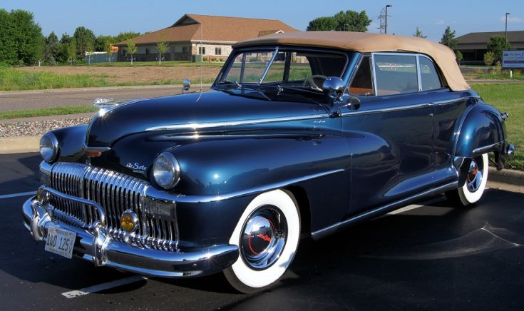 1947 DeSoto Custom Convertible kabrió, osztott ablakos kék kabrió barnás ponyvatetővel, elölnézet, oldalnézet, balról döntve, alulról felfelé fotózva, fehérfalú gumival, háttérben ranch és hatalmas ház