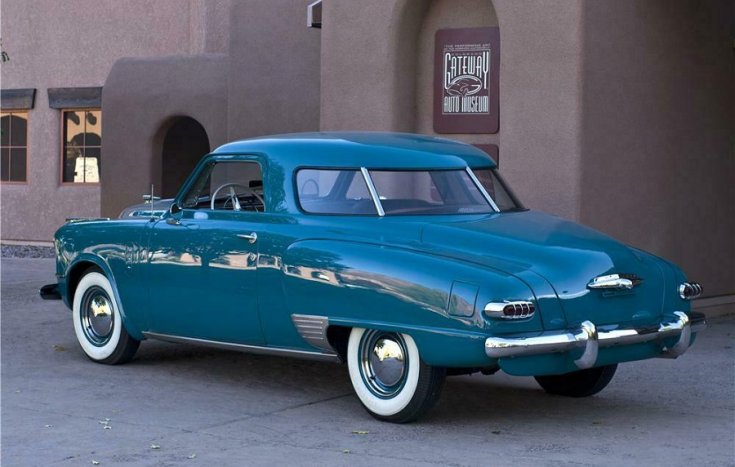 1948 Studebaker Commander Starlight Coupé, kék kupé, azúrkék, fehérfalú gumival, hátulnézet, oldalnézet, balról döntve, alulról felfelé fotózva, háttérben barna épület
