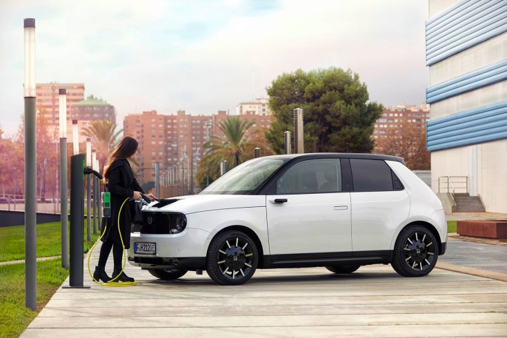 Fiatal hölgy a kezében töltőkábellel egy Honda E előtt