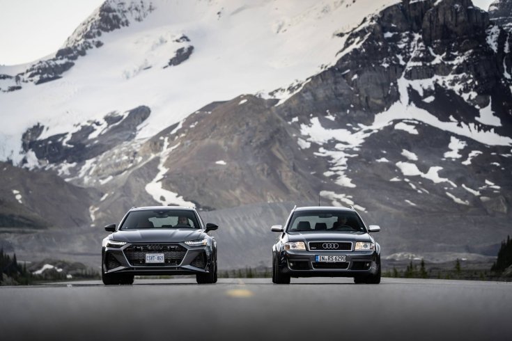 FOtón két havas hegyek előtt aszfalton álló szürke Audi RS 6 Avant autóról. A baloldali a C5-ös a jobboldali a C8-as generáció