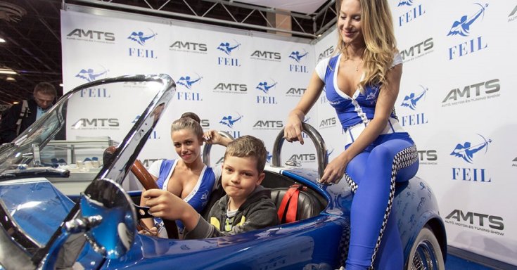 Kisfiú ül az autóban, mellette pedig két hostess az AMTS fesztiválon