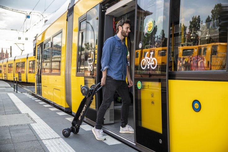 Egy férfi száll fel a villamosra az Audi E-Tron elektromos rollerrel kezében
