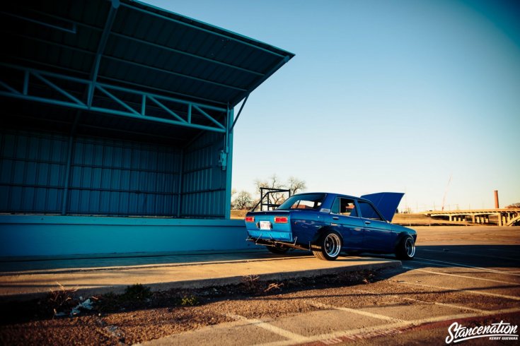 Wes Glockzin 1969-es Datsun 510 Bluebirdje, hátulról, 45 fokból, kék színben, naplementében egy hangárnál