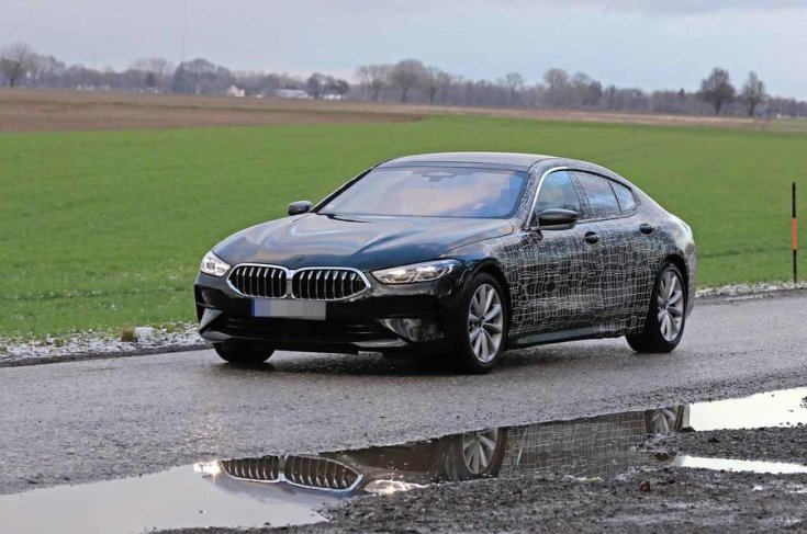 A 2019-es BMW 8 Gran Coupé álcázott prototípusa szemből fotózva egy réten