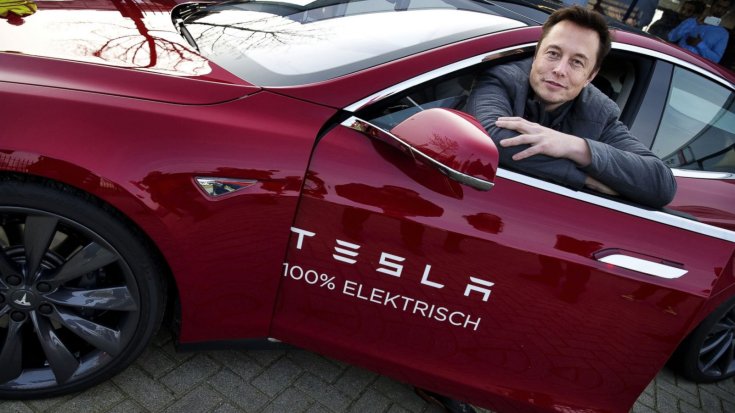 Elon Musk egy Tesla Model S ajtajára támaszkodva mosolyog