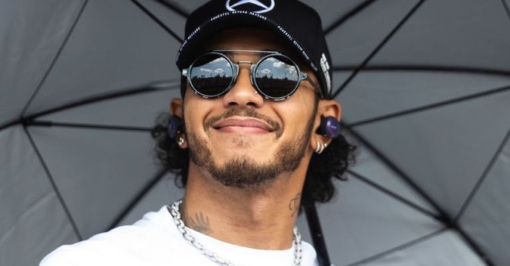 Hamilton mosolyog napszemüvegben egy esernyő alatt