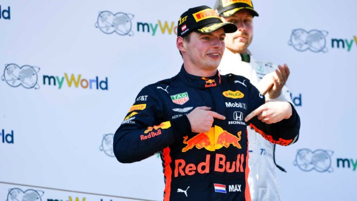 Max Verstappen egy győzelem után a Honda emblémára mutat. háttérben Bottas