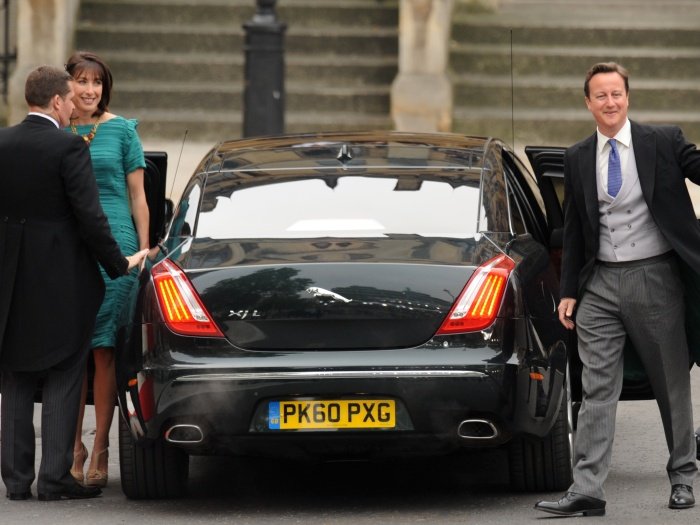 Fekete színű Jaguar XJ hátulról, mellette aza utóból kiszálló David Cameron miniszterelnök