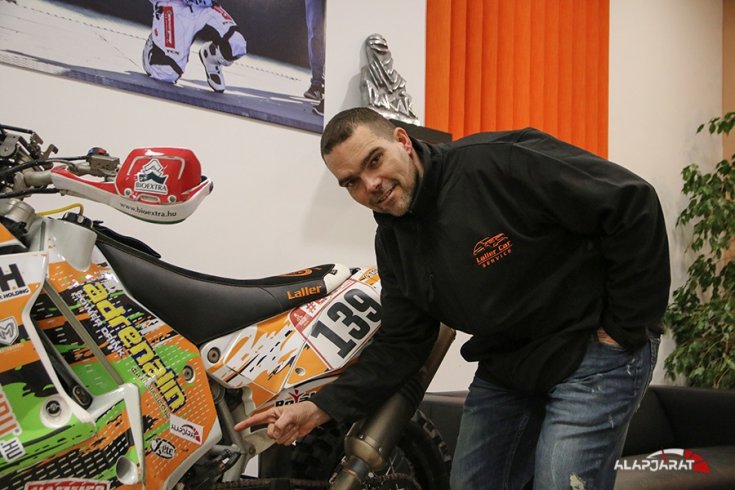 Laller a motorja mellett, amin az Alapjárat logójára mutat