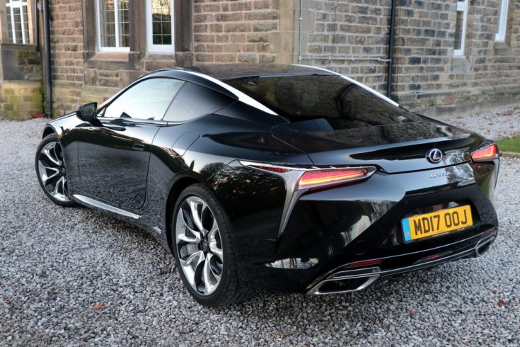 Fekete fényezésű, Lexus LC500-as egy téglaház előtt, hátulról, oldalról