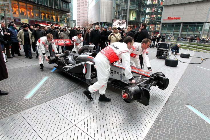 Mclaren szerelők tolják be a tér közepére az istálló szétszedett autóját