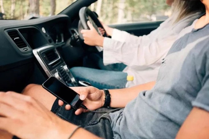 mobilját kézben tartó oktató, miközben a tanulóvezető vezet