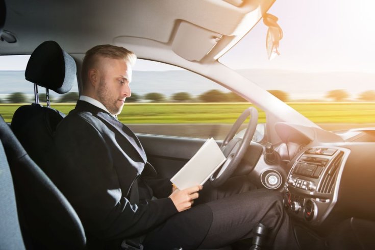 Önvezető autó volánja mögött ülő férfi könyvet olvas