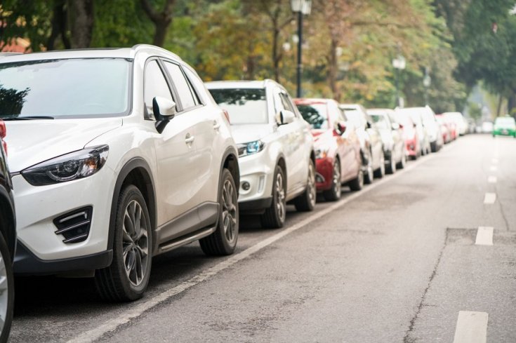 autók párhuzamosan parkolnak egy kétsávos út mentén