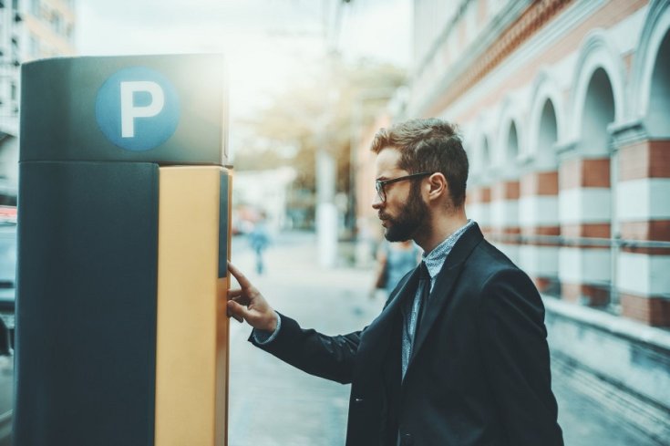 parkolóautomatát használó öltönyös férfi
