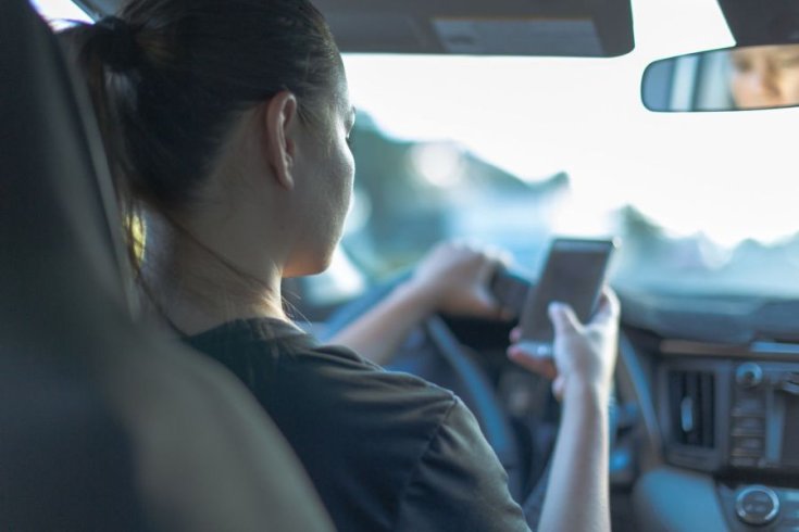 balesetveszélyesen vezetés közben telefonját nyomkodó hölgy egy nem önvezető autóban
